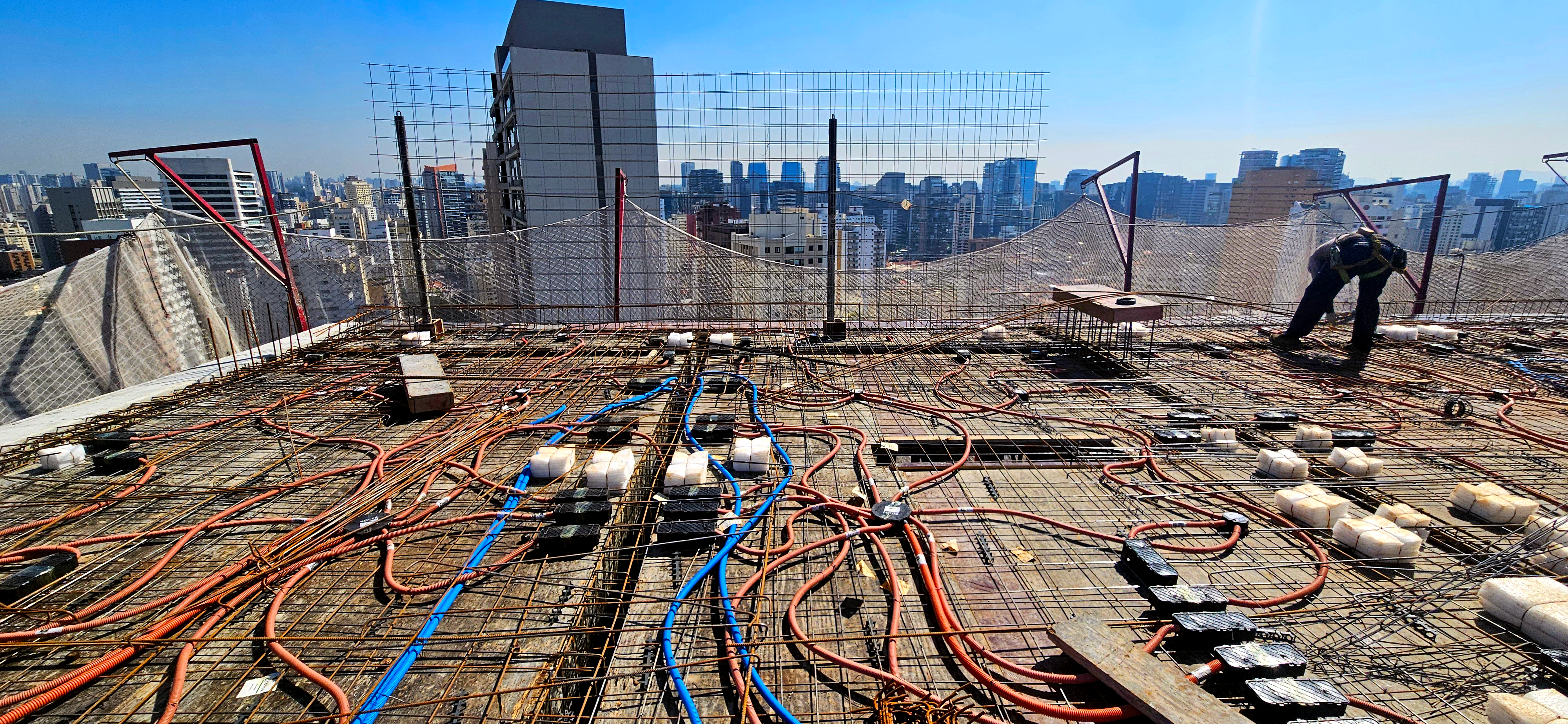 Eletrodutos corrugados laranja e azul instalados na armação de laje de edifício antes da concretagem